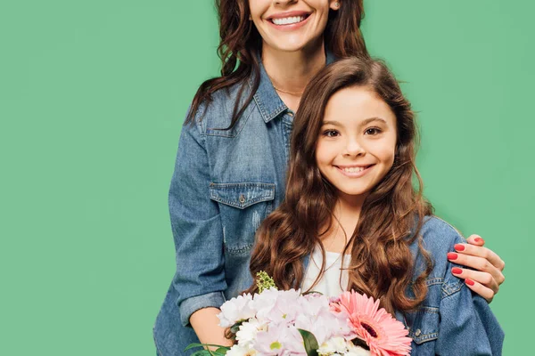 Mère embrassant fille heureuse avec bouquet de fleurs isolé sur vert — Photo de stock