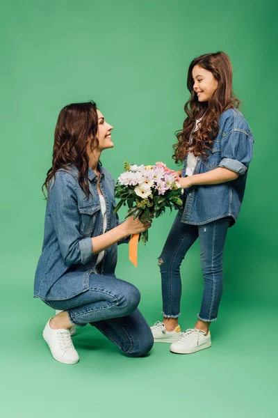 Lächelnde Mutter mit Blumen und entzückender Tochter auf grünem Hintergrund — Stockfoto