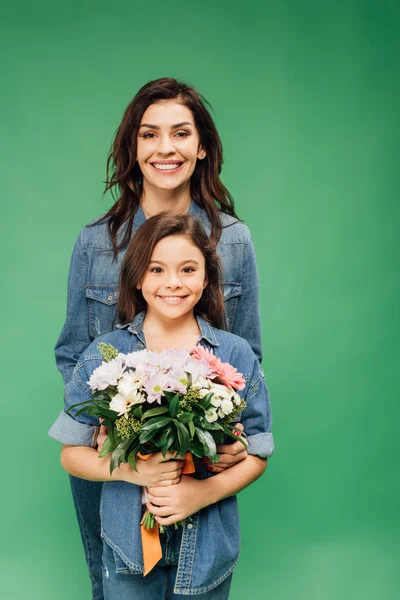 Mãe e filha olhando para a câmera e segurando buquê de flores isolado no verde — Fotografia de Stock