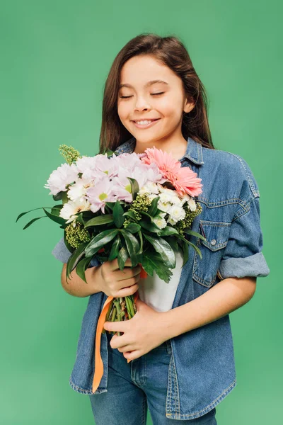 Cute child with eyes closed holding flower bouquet isolated on green — Stock Photo