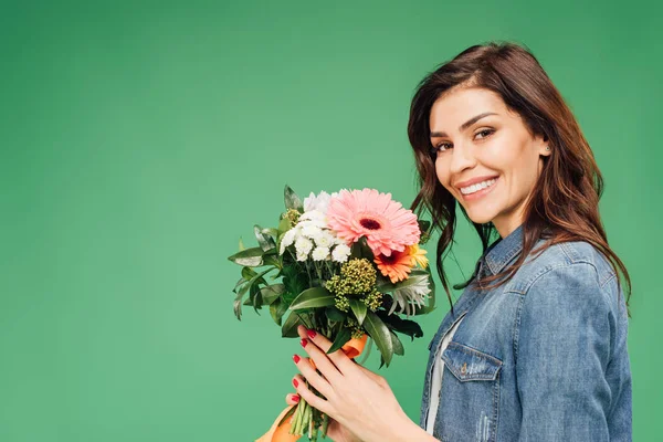 Hermosa mujer sonriente sosteniendo ramo de flores y mirando a la cámara aislada en verde - foto de stock