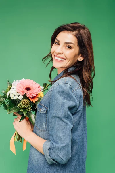 Attractive woman holding flower bouquet and looking at camera isolated on green — Stock Photo