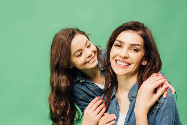 Smiling mother and daughter in denim embracing isolated on green — Stock Photo
