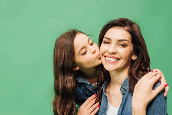 Niedliche Tochter küsst lächelnde Mutter Wange isoliert auf grün — Stockfoto