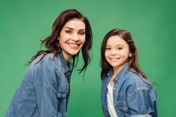 Happy mother and daughter in denim looking at camera isolated on green — Stock Photo