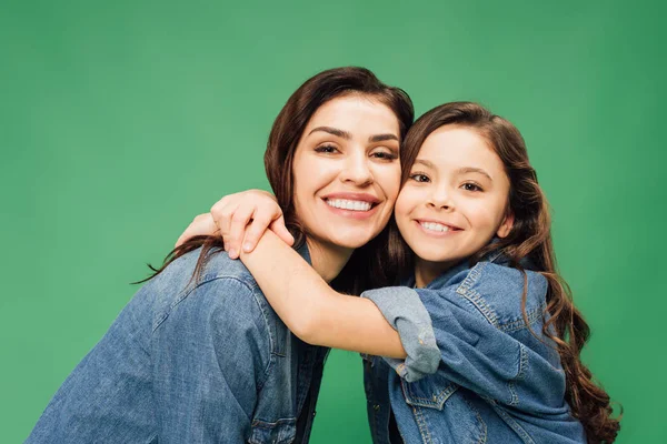 Щаслива мати і дочка обіймаються і дивляться на камеру ізольовано на зеленому — стокове фото