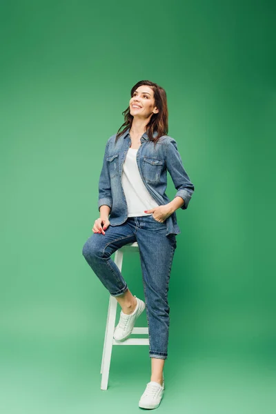 Hermosa mujer sonriente en denim y mano en el bolsillo sentado en la silla - foto de stock