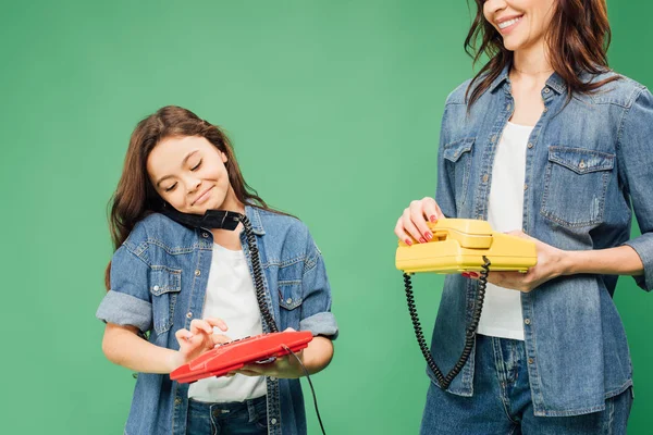 Mutter und lächelnde Tochter halten alte Telefone isoliert auf Grün — Stockfoto