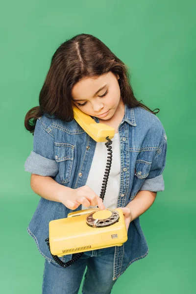 Niedliches Kind spricht auf gelbem Telefon isoliert auf grünem — Stockfoto