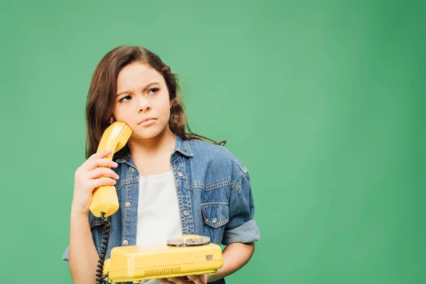 Criança confusa em ganga segurando telefone vintage isolado em verde — Fotografia de Stock