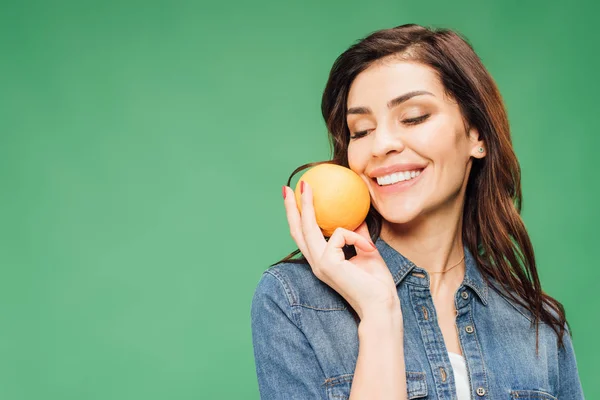 Beautiful smiling woman in denim holding orange isolated on green — Stock Photo