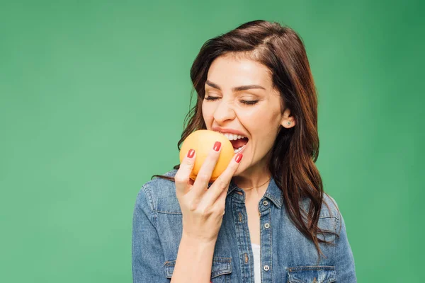 Frau in Jeans beißt Orangenfrucht auf Grün — Stockfoto