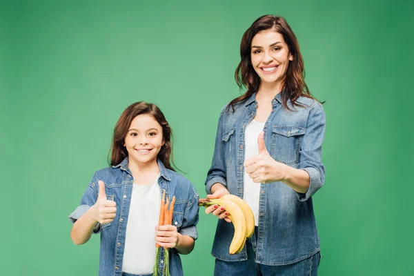 Mother and daughter showing thumbs up  and holding bananas with carrots isolated on green — Stock Photo