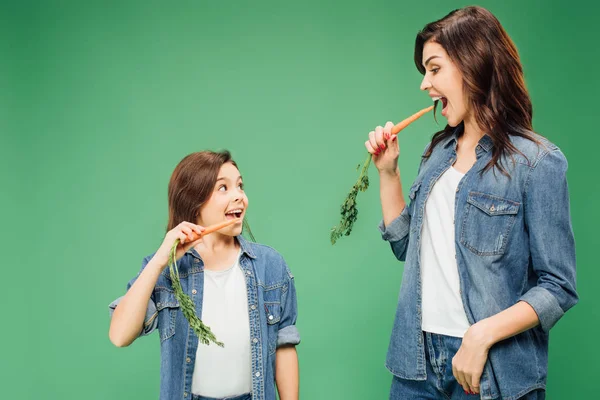 Mãe e filha comendo cenouras e olhando uns para os outros isolados em verde — Fotografia de Stock