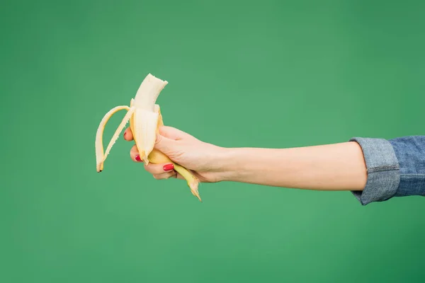 Vista recortada de la mujer sosteniendo la mitad de plátano en la mano aislado en verde - foto de stock