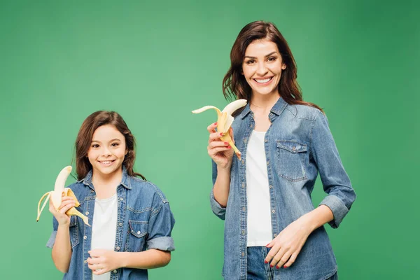 Glückliche Mutter und Tochter halten Bananen isoliert auf Grün — Stockfoto