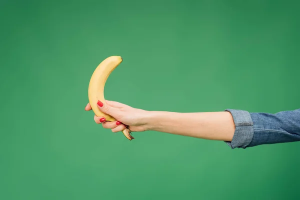 Cropped view of woman holding banana in hand isolated on green — Stock Photo