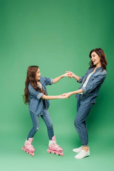 Tochter in Rollerblades hält Händchen mit glücklicher Mutter auf grünem Hintergrund — Stockfoto