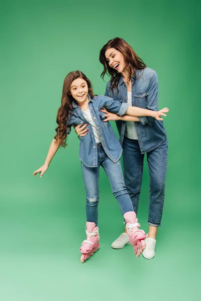 Sonriente madre enseñando hija patinaje sobre fondo verde - foto de stock