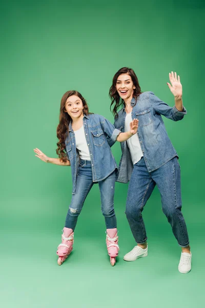 Hija en patines gesticulando con las manos con feliz madre sobre fondo verde - foto de stock