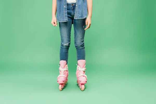 Cropped view of child wearing denim and pink rollerblades on green background — Stock Photo