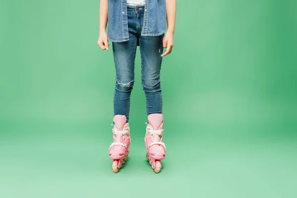 Vista recortada del niño con vaqueros y patines de color rosa sobre fondo verde - foto de stock