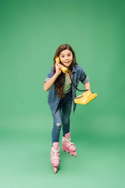 Child rollerblading and talking on vintage telephone on green background — Stock Photo