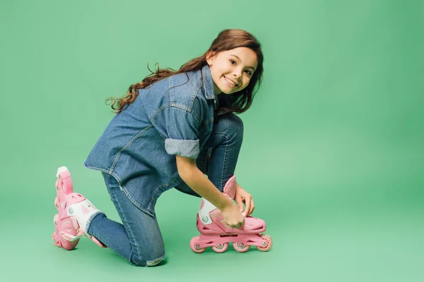 Cute child putting on rollerblades and looking at camera on green background — Stock Photo