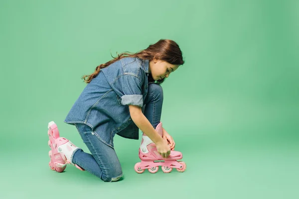 Child in denim putting on roller blades on green background — Stock Photo