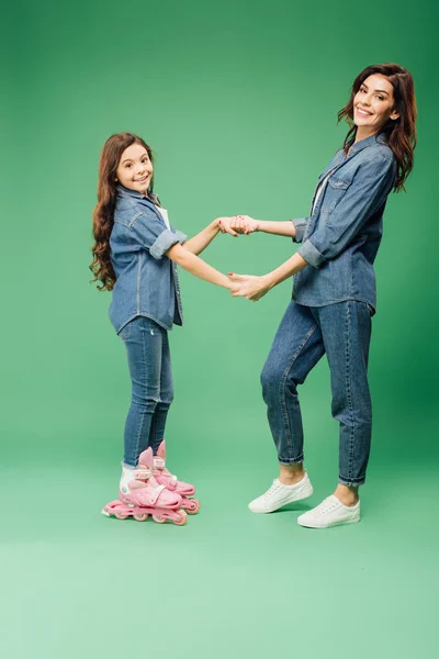 Adorable daughter in roller blades holding hands with mother on green background — Stock Photo