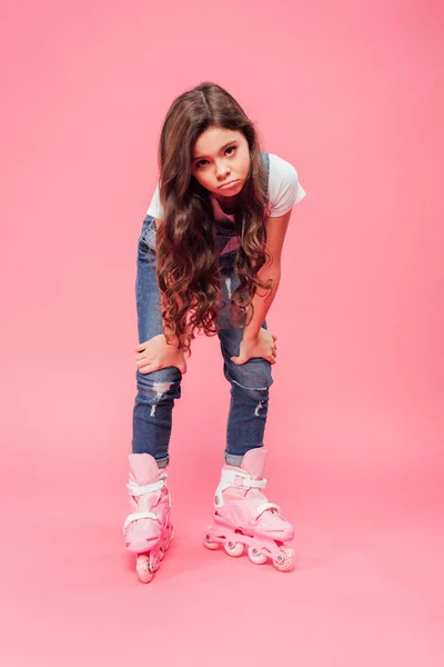 Upset child in overalls and rollerblades pouting lips and looking at camera on pink background — Stock Photo