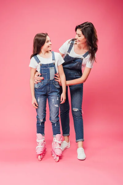 Sonriente madre abrazando hija en patines sobre fondo rosa - foto de stock