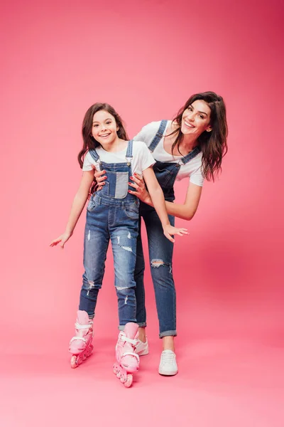 Mãe sorridente ensinando filha patinando em fundo rosa — Fotografia de Stock