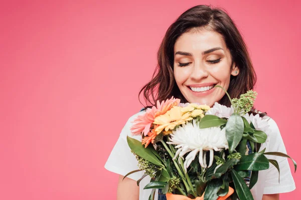 Hermosa mujer con los ojos cerrados sosteniendo ramo de flores aislado en rosa - foto de stock