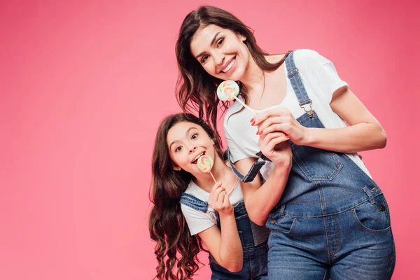 Sorridente madre e figlia in possesso di lecca-lecca isolati su rosa — Foto stock