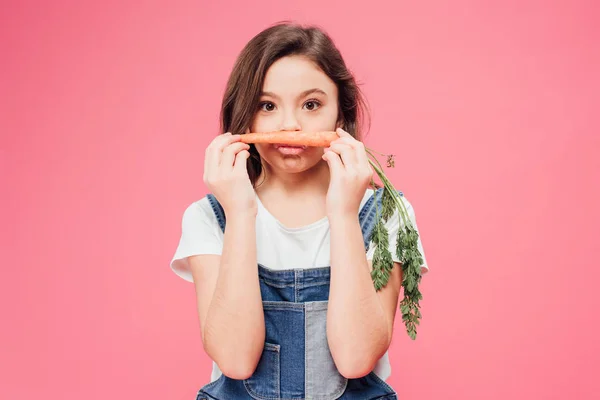 Lustiges Kind, das Karotte in Mundnähe hält, isoliert auf rosa — Stockfoto