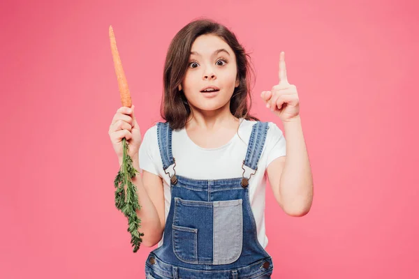 Niño feliz mostrando gesto de idea y sosteniendo zanahoria aislada en rosa - foto de stock