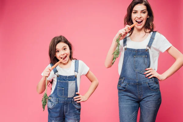 Mutter und Tochter essen frische Möhren isoliert auf rosa — Stockfoto