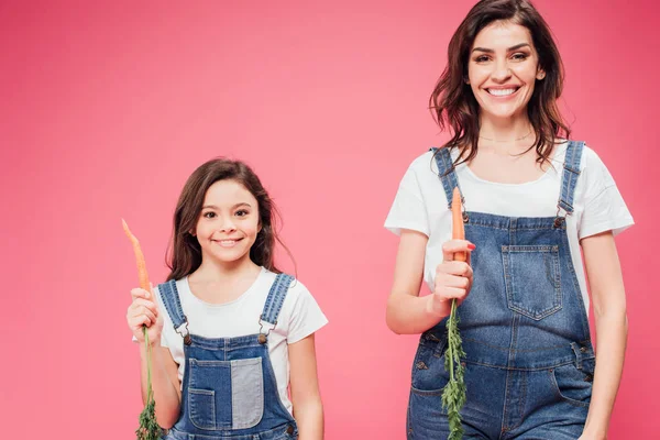 Mother and daughter holding fresh carrots isolated on pink — Stock Photo