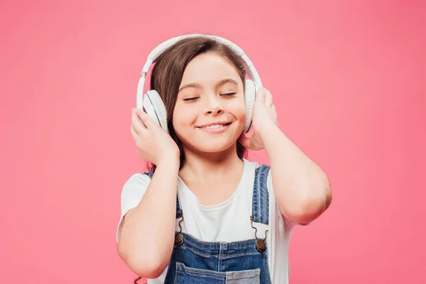 Niño sonriente escuchando música en auriculares aislados en rosa - foto de stock