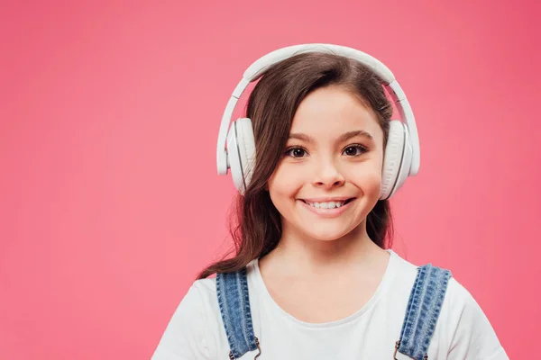 Niño sonriente escuchando música en auriculares aislados en rosa - foto de stock