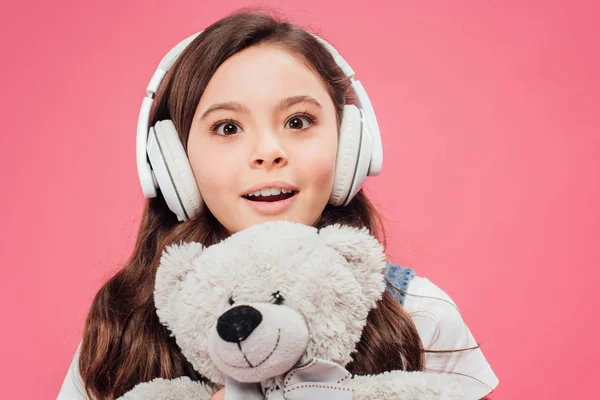 Niño excitado en auriculares con osito de peluche aislado en rosa - foto de stock