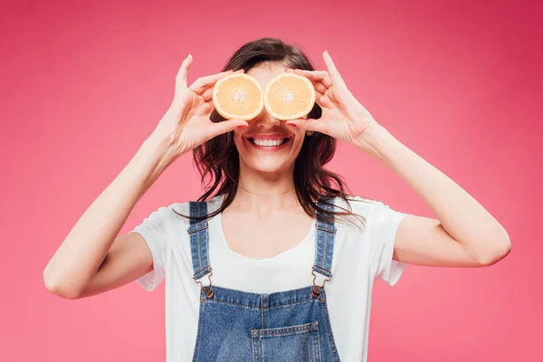 Smiling woman holding oranges over eyes isolated on pink — Stock Photo
