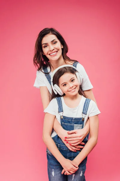 Madre abrazando hija en auriculares aislados en rosa - foto de stock