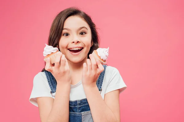 Bambino eccitato che tiene cupcake in mani isolate su rosa — Foto stock