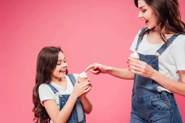 Mother touching sweet cream on cupcake of daughter isolated on pink — Stock Photo