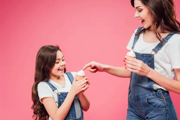 Madre tocando crema dulce en cupcake de hija aislado en rosa - foto de stock