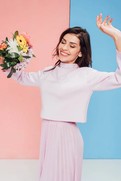 Schöne Frau mit Blumenstrauß und Tanz auf blauem und rosa Hintergrund — Stockfoto