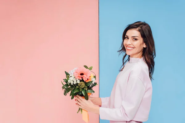 Bella donna che tiene bouquet e sorride alla macchina fotografica su sfondo blu e rosa — Foto stock