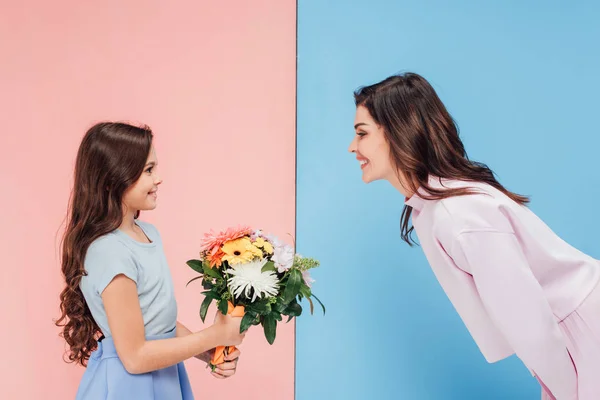 Чарівна дитина дарує букет привабливій жінці на синьо-рожевому фоні — стокове фото